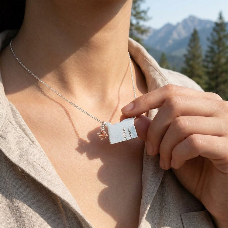 Close-up of sterling silver Oregon Pride Necklace with sunstone pendant on model's neck, natural outdoor background with pine trees.
