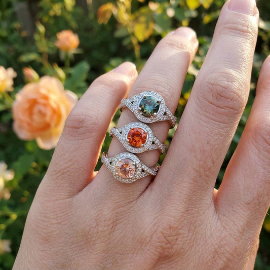 Close-up of a petite white gold wedding ring with Oregon Sunstone and diamond halo on a natural light background with greenery and sunlight.
