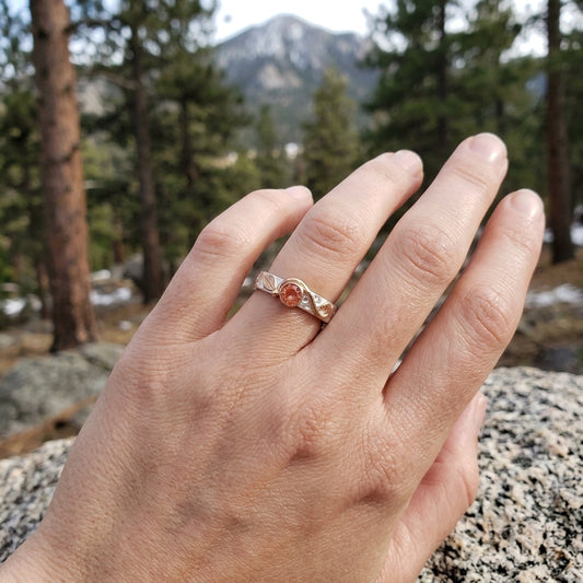 Close-up of the ring focusing on rose gold leaf detailing and Oregon Sunstone, with a softly blurred natural background.