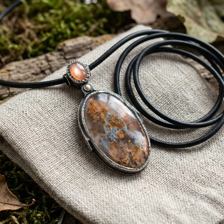Close-up of the Sunstone Nebula pendant on textured fabric, showing craftsmanship and intricate gemstone patterns with natural lighting.