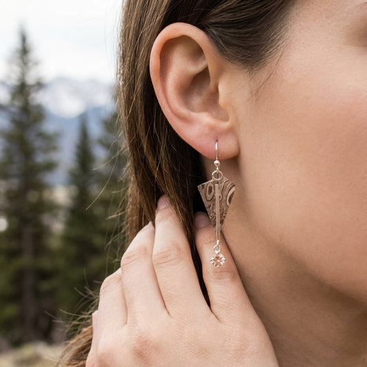 Close-up of model's ear and hand showcasing intricate copper and silver 'Mokume-Gane Kite' earrings with Oregon Sunstone.
