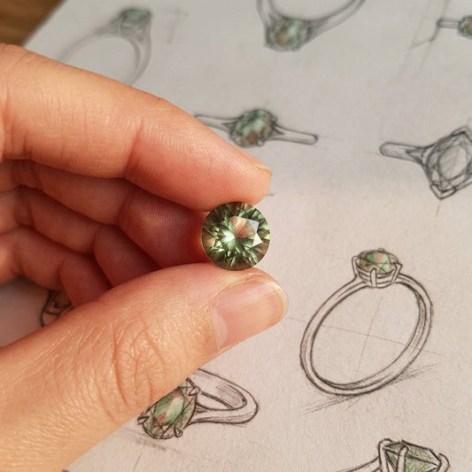 Stylized scene of a hand gently holding a faceted Oregon Sunstone highlighting micro-texture and shimmering green and peach hues.