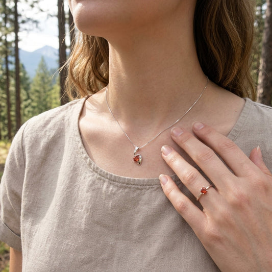 Full-body image of a model outdoors showcasing a gold or silver Oregon Sunstone pendant and ring, with a pine and mountain landscape in soft natural light.