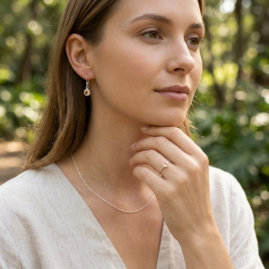 Full-body shot of a female model in casual attire outdoors wearing subtle silver sunstone earrings and a simple necklace with natural scenery.