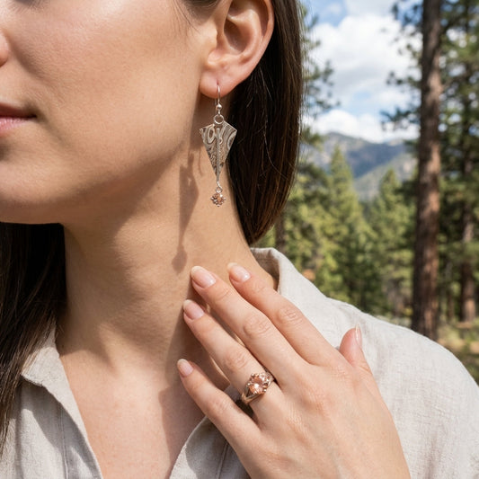 Full-body shot of model outdoors wearing copper and silver 'Mokume-Gane Kite' earrings with Oregon Sunstone, set in a natural mountain scene.