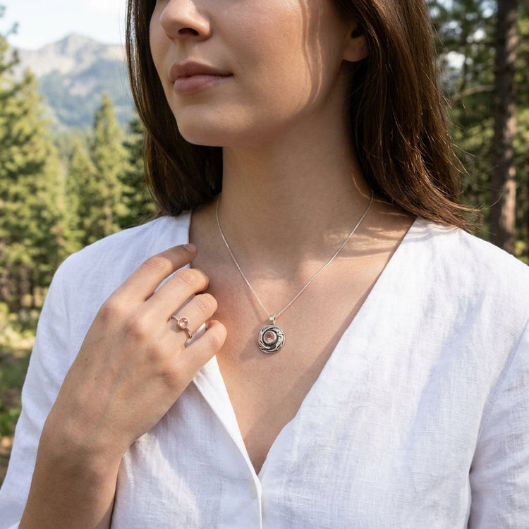 Full-body view of a model outdoors wearing a small silver otter pendant with sunstone on her collarbone, in a natural pine and mountain setting.