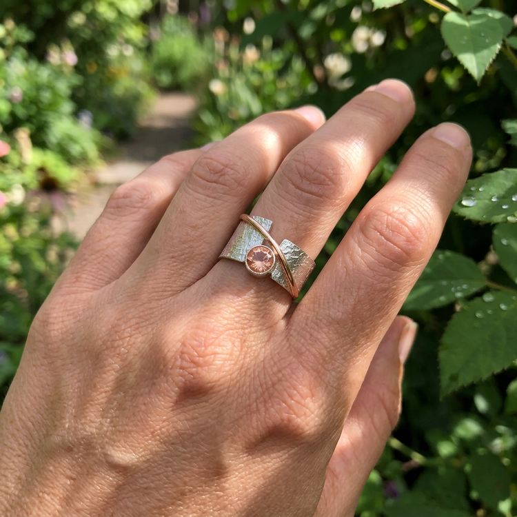 Full hand pose featuring the Alya Star Sunstone Ring on the middle finger, outdoors with lush garden background and warm sunlight.