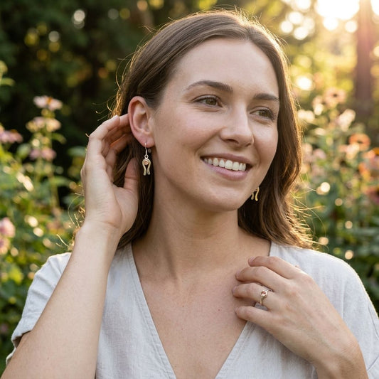 Scene of a woman in a shaded garden at golden hour wearing delicate earrings with peach Oregon Sunstone.