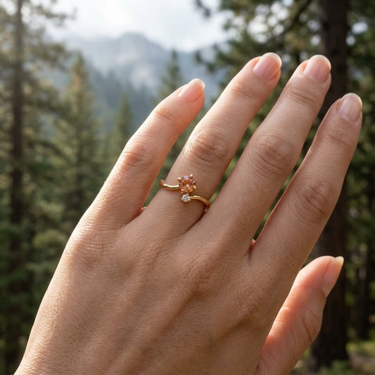 Close-up of a hand with the gold Oregon Sunstone ring, placed on the palm with pine trees and misty mountains in the background, highlighting the gemstone's fiery glow.