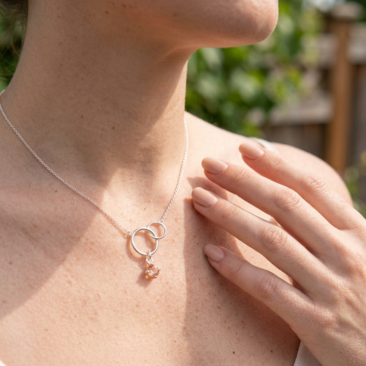 Elegant hand with manicured nails wearing Silver Harmony Necklace outdoors, sunstone glowing softly in sunlight, emphasizing jewelry details.
