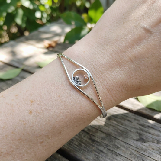 Full wrist shot of Mini Mountain Cuff Bracelet on a medium wrist outdoors, showing its delicate split cuff design, sterling silver texture, and vibrant Sunstone.