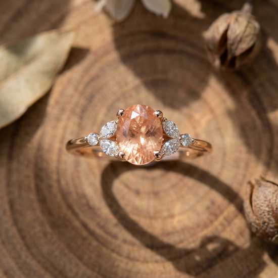 Close-up of the Mkayla Sunstone Engagement Ring in rose gold with peach champagne sunstone and diamond accents on a wooden surface.
