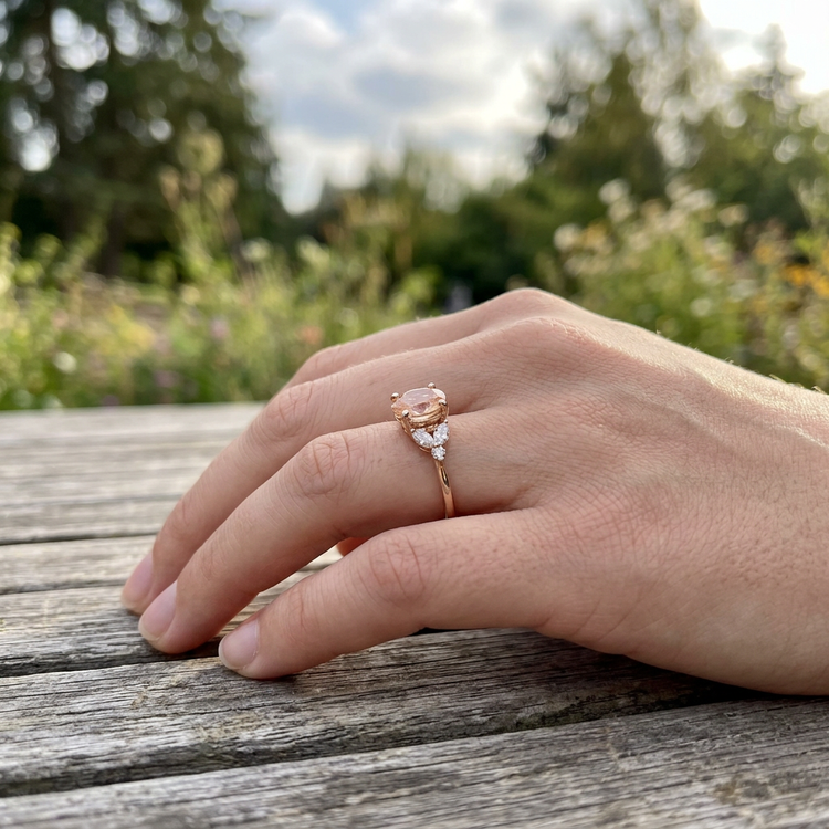 Worn Mkayla Sunstone Engagement Ring on a hand outdoors with greenery, showcasing its petite design and rose gold band.