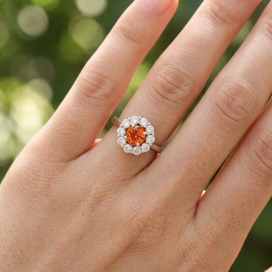 Model showcasing a petite 14K white gold diamond halo ring set with vibrant orange sapphire, natural outdoor background emphasizes elegance.