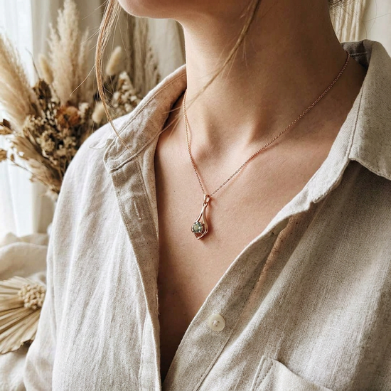 Close-up of the gold necklace chain and lobster clasp on light wooden surface, emphasizing craftsmanship and fine details of the jewelry.