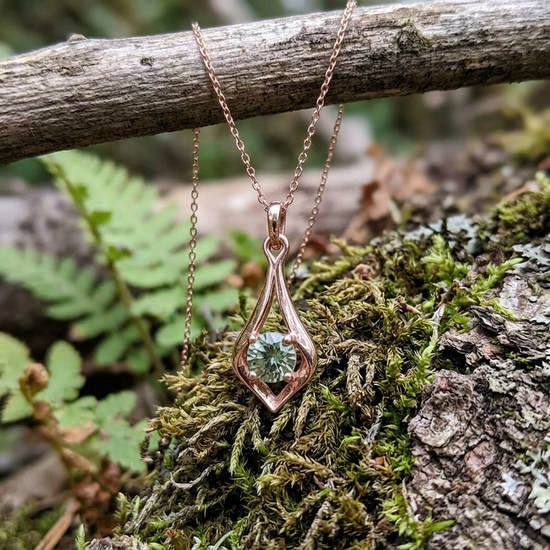 Pendant hanging from a hook in a natural outdoor setting with moss and bark background, highlighting the petite size and organic beauty of the sunstone.