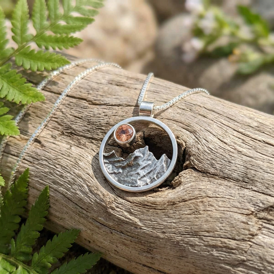 Sterling silver mountain necklace with Oregon Sunstone resting on slate stone, showcasing detailed silver texture and organic design.