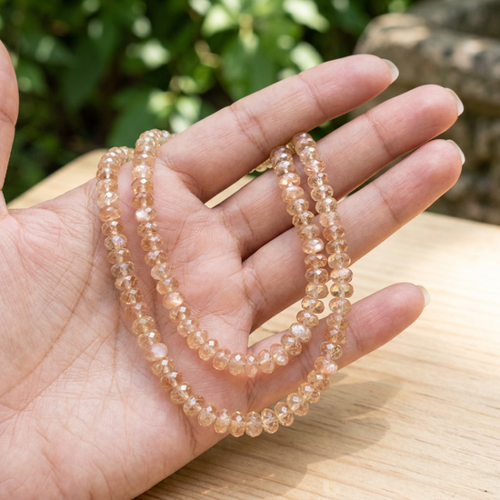 Two Oregon Sunstone bead strands loosely arranged on a hand outdoors, highlighting their subtle size variation and harmonious champagne and pink hues.