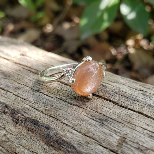 Close-up of Odyssey Sunstone Cabochon Ring showing 9x7mm peach Oregon Sunstone with Schiller, set in Continuum Sterling Silver, with natural lighting and weathered wood background.