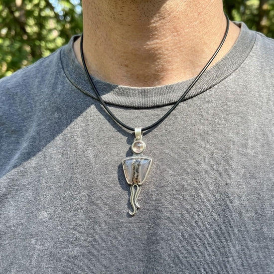 Close-up of a handcrafted sterling silver necklace with Montana Agate and Oregon Sunstone pendant, worn by a man outdoors with green foliage background.