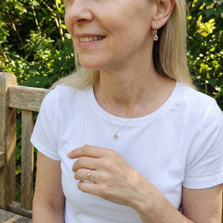 Casual outdoor scene of a woman seated on a wooden bench wearing silver earrings and a delicate necklace with natural lighting.