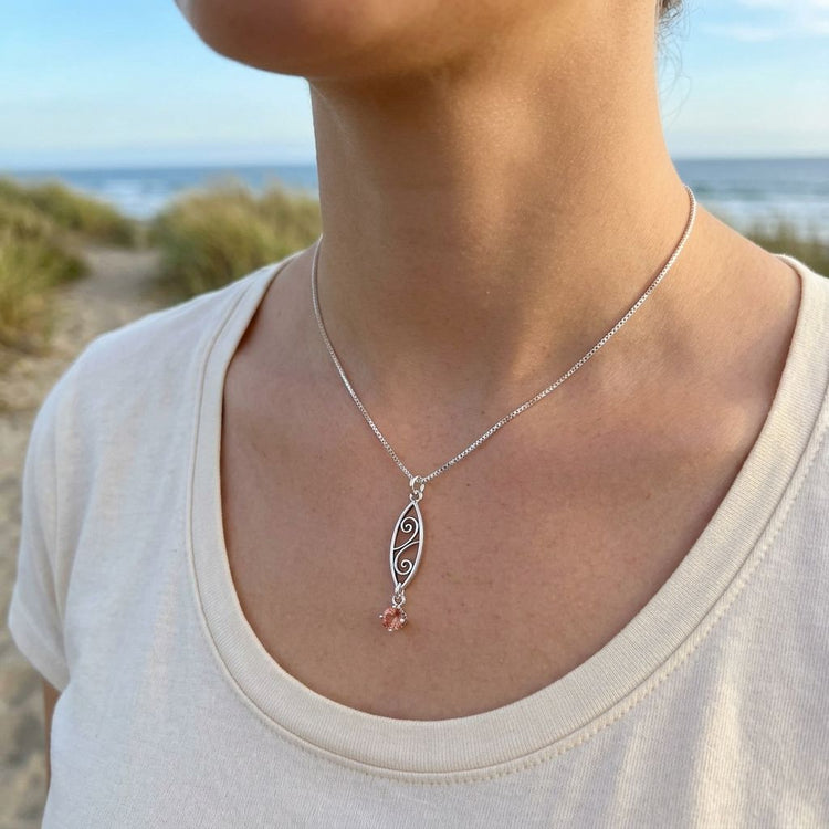 Female model outdoors wearing delicate sterling silver Sunstone necklace with scroll design on a natural landscape background.