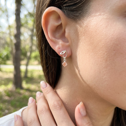 Beautiful, well-manicured hand displaying sterling silver Twinleaf earring with Oregon Sunstone in a casual outdoor scene with soft natural light and greenery.