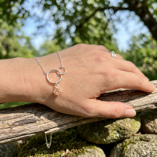 Model outdoors wearing Silver Harmony Necklace, gently holding wildflowers, with sunstone pendant prominently displayed in natural daylight.
