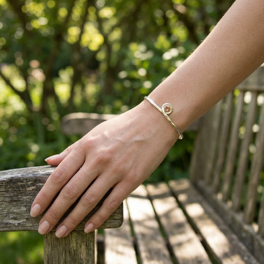 Full-body shot of a model with a silver Oregon Sunstone cuff bracelet, resting on a wooden bench in a sunny park or garden setting, emphasizing natural beauty.