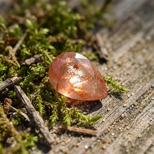 Overhead view of peach Schiller sunstone nestled among moss, twigs, and sand on rustic wood, illuminated by soft morning sunlight highlighting its intrinsic beauty.