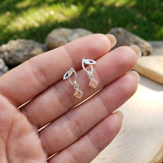 Close-up of hand with fingers extended wearing sterling silver Twinleaf earring with Oregon Sunstone in natural sunlight, emphasizing delicate size and sparkle.