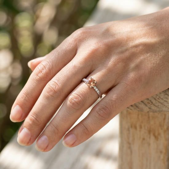 Side view of a hand wearing the Hearts Afire engagement ring against a natural outdoor background with soft sunlight.