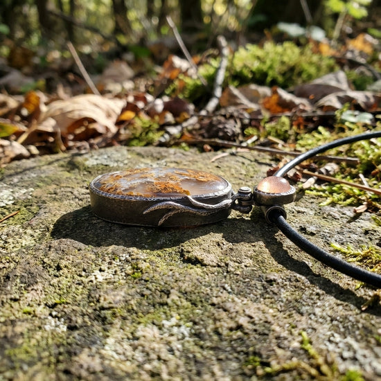 Side view of the Sunstone Nebula pendant displayed on weathered stone, emphasizing handcrafted textures and celestial agate patterns.