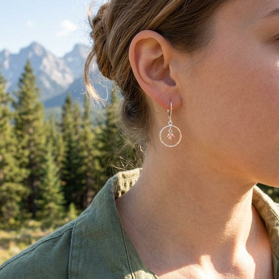 Silver Saturn Earring worn on a model’s ear in an outdoor setting with pine trees and mountains, showing the earring’s delicate movement and shine.