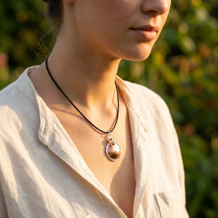 Model wearing the Copper-Silvermoon Necklace with Sunstone on a leather cord, outdoor setting during golden hour highlighting warm tones.