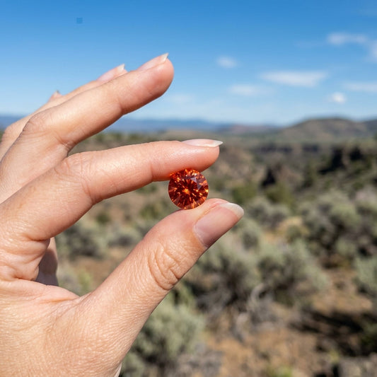 Vivid orange Oregon Sunstone in a display box with rugged desert background, capturing fiery sparkle under natural sunlight.