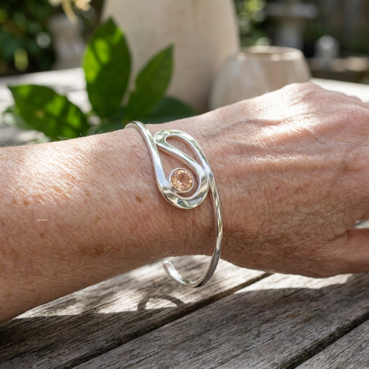 Person wearing the 'Ebb & Flow' double sunstone cuff bracelet outdoors, showcasing its adjustability and vibrant sunstone in natural light.