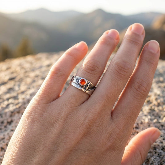 Wide-angle view of a sterling silver mountain-lover's ring with a 4mm Sunstone on an elegant hand in a warm natural setting, emphasizing the ring's shape and color variation.