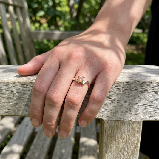 Full view of a person wearing the elegant Sunstone Solitaire Ring on their hand, casually resting outdoors against a wooden surface.
